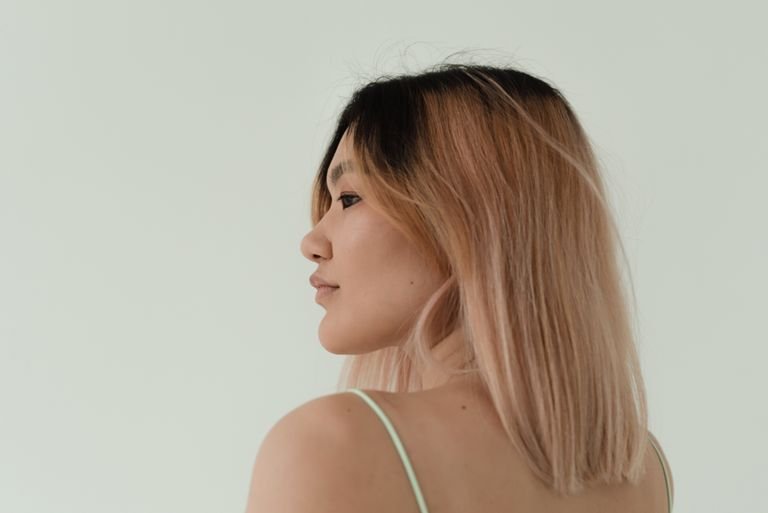 A side view portrait of a woman with light pink balayage hair on a minimalistic background.