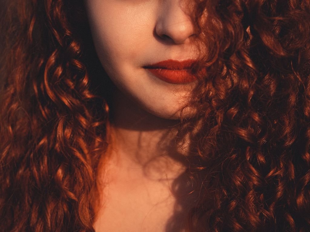 Unrecognizable beautiful female with dark reddish fluffy hair and vivid red lips in daylight