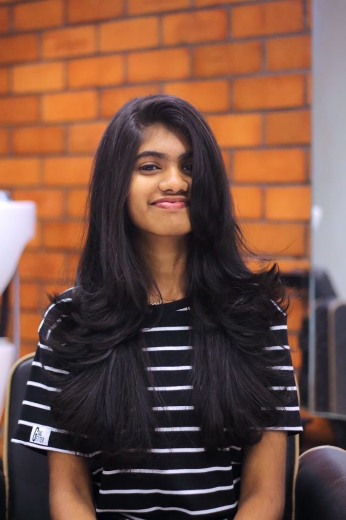 A cheerful young woman with long hair sitting in a salon, smiling warmly.