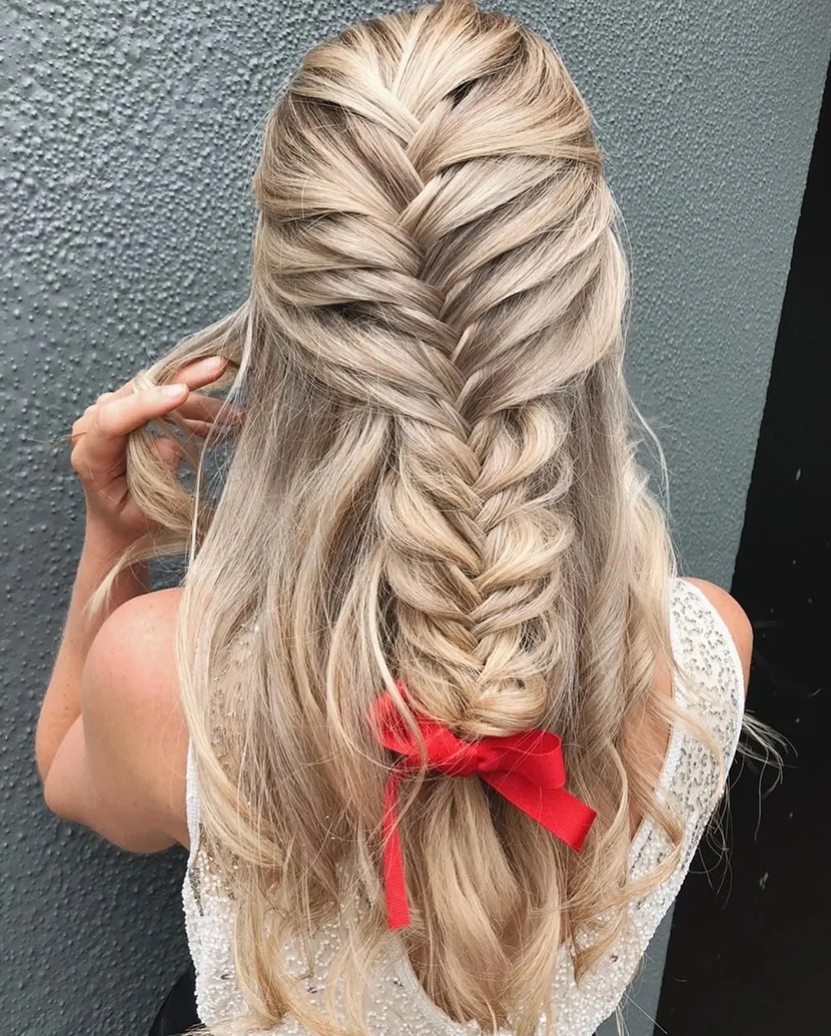 Half-up fishtail braid tied with a bright red ribbon bow