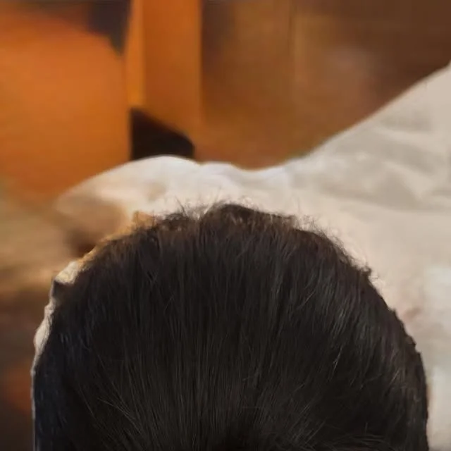 Back view of a woman wearing a sleek high bun with smooth dark hair.