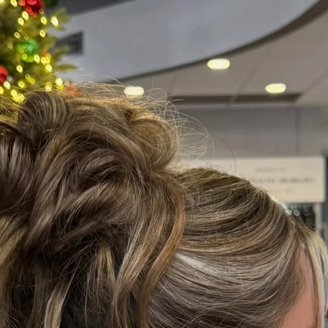 Side view of a voluminous textured bun with loose tendrils beside a decorated Christmas tree.