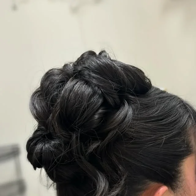 Voluminous twisted bun hairstyle with soft curled pieces framing the face.