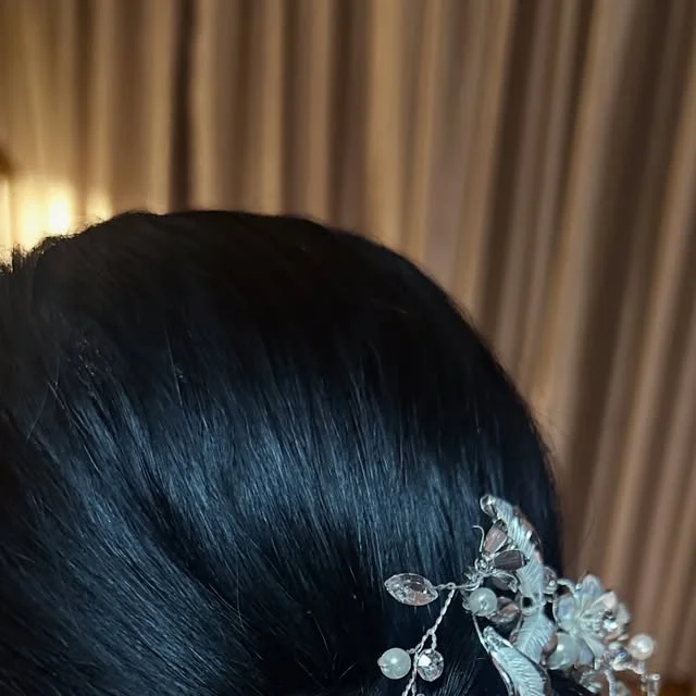 Low twisted bun adorned with a silver crystal and pearl hair vine.