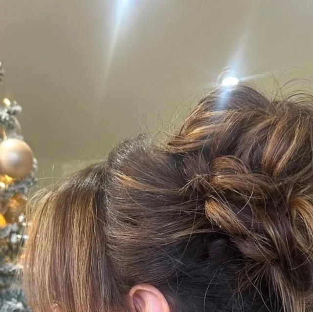 Side braided messy bun with dark brown and blonde highlighted hair.