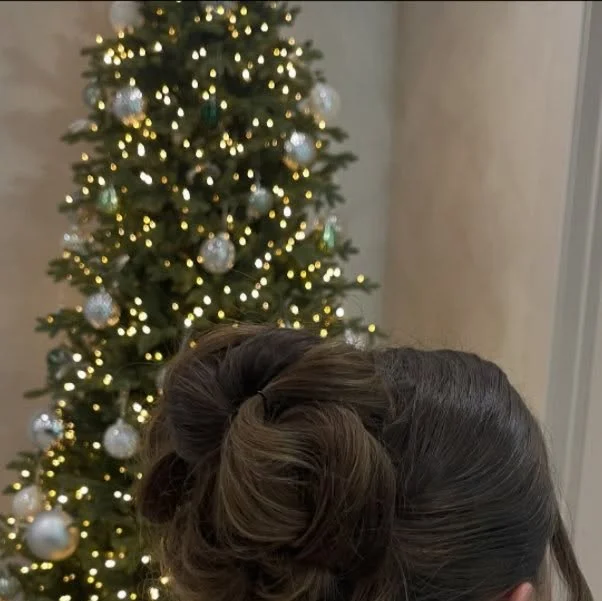 Large twisted bun with loose curled tendrils in front of a Christmas tree.