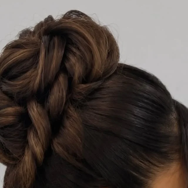High braided bun with twisted sections and a curled face framing tendril.