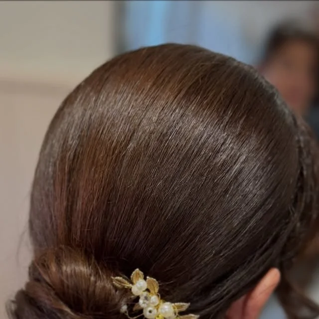 Polished low bun secured with a gold and pearl floral hair pin.