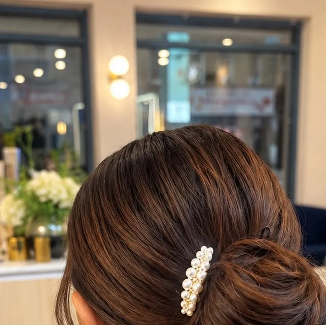 Classic low bun styled with a decorative pearl hair clip on the side.