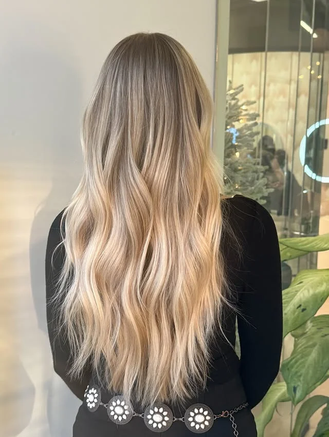 Back view of long blonde hair styled in voluminous waves with a decorated Christmas tree in the background.