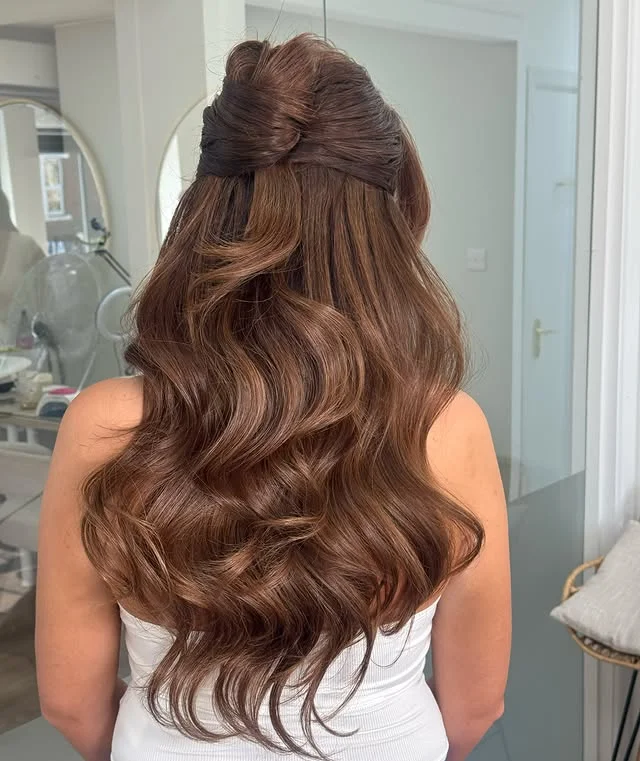 Back view of long highlighted brown hair in a half-up twisted style with soft waves.