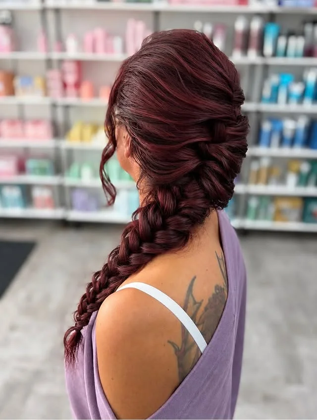 Side view of burgundy-red hair swept into an updo that flows into a thick fishtail braid.