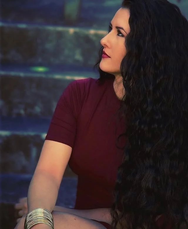 Portrait of a woman with long dark curly hair falling over her shoulders.