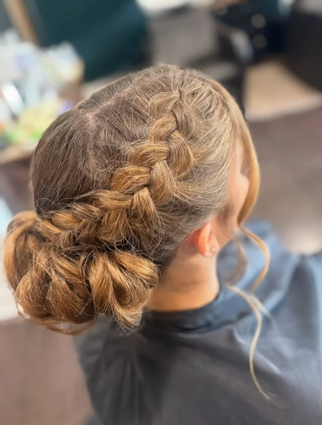Close side view of light brown hair braided and wrapped into a low bun at the nape.