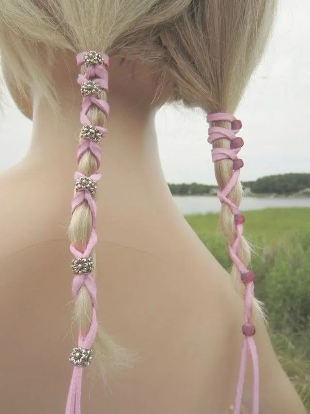 Close rear view of two blonde braids woven with pink ribbon and decorative beads.