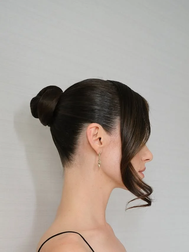 Side profile of dark hair smoothed into a polished high bun with a soft face-framing tendril.