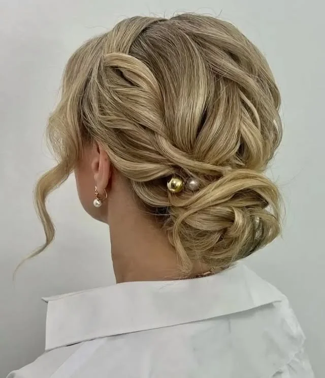 Back view of a blonde low chignon decorated with gold and pearl hairpins.