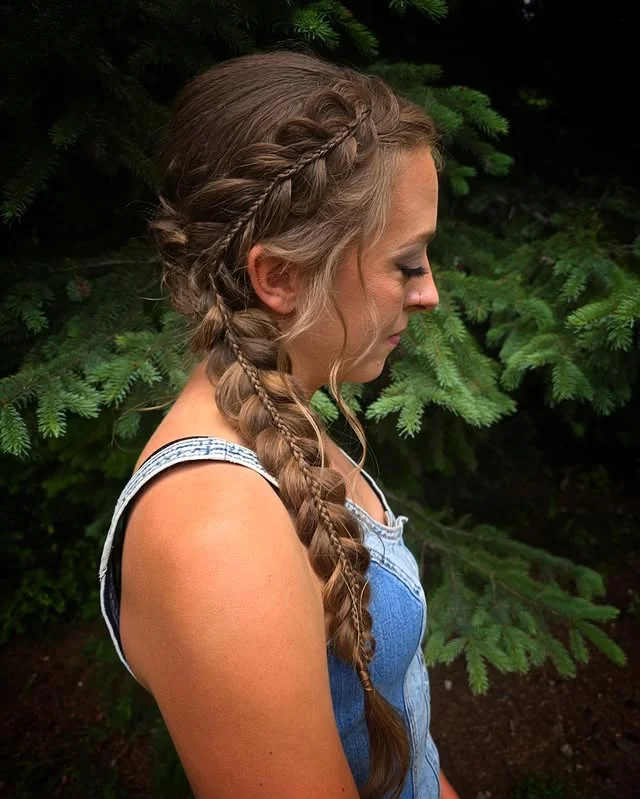 Side view of long brown hair styled in a double Dutch braid against green foliage.