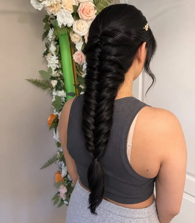 Back view of long black hair in a sleek fishtail braid with a small gold hair accessory at the crown.