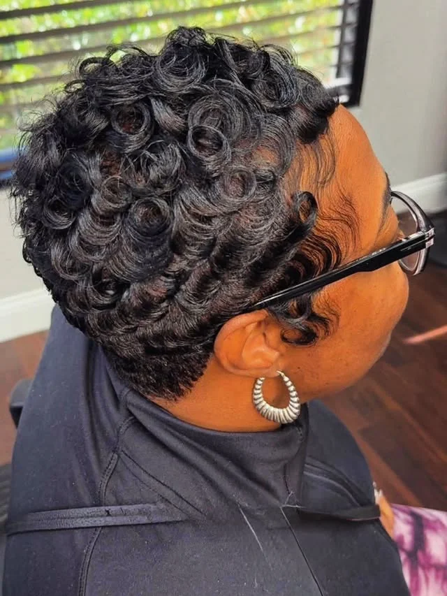 Close view of a woman with a short, tightly coiled curly crop and a silver hoop earring.