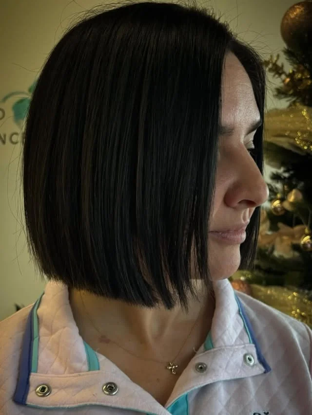 Side profile of a woman with a sleek straight black bob, standing in front of a Christmas tree.