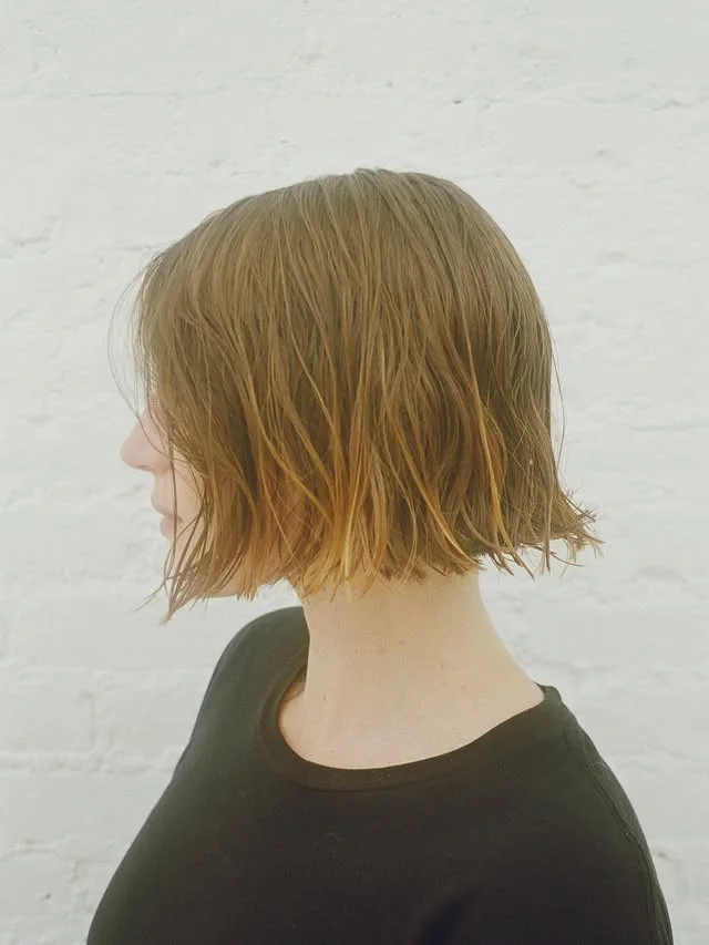 Side profile of a woman with a wet-look chin-length brown bob against a plain white wall.