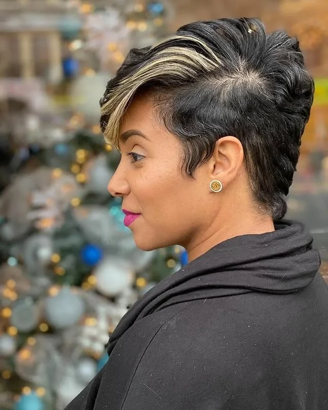 Side profile of a woman with a dark pixie cut with blonde highlights, with a blurred Christmas tree behind her.