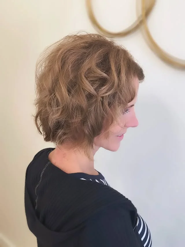 Side view of a woman with a short wavy brown bob with soft natural volume.
