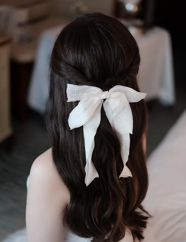 Half-up wavy hair secured with a large sheer cream ribbon bow