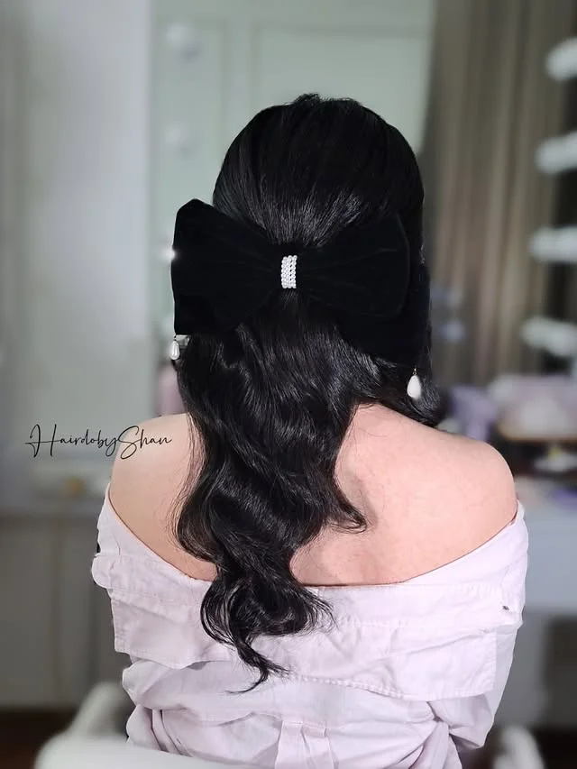 Dark wavy half ponytail tied with a black velvet bow with a rhinestone center