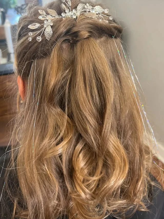 Half-up wavy hair adorned with a crystal and pearl hair vine and tinsel strands