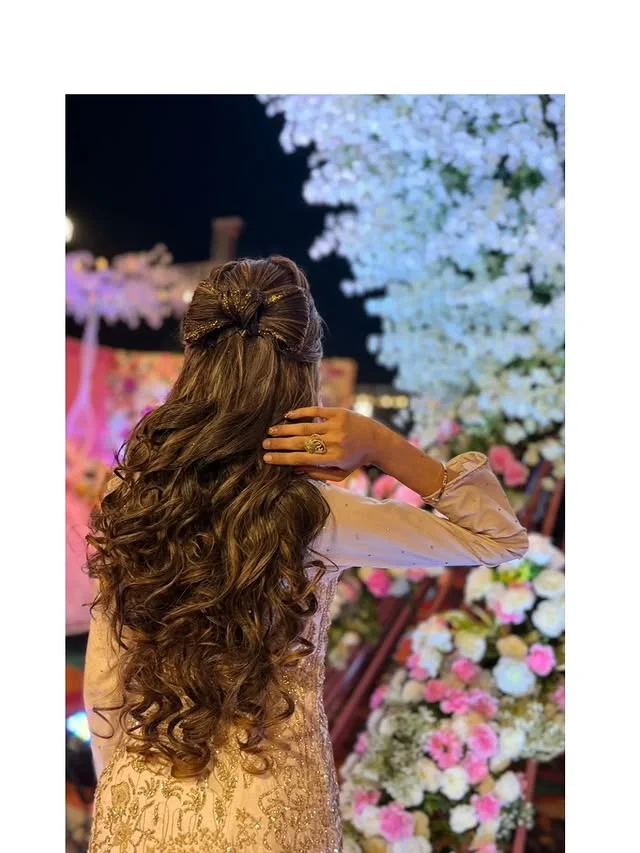 Voluminous brown curls in a half-updo finished with a glittery bow