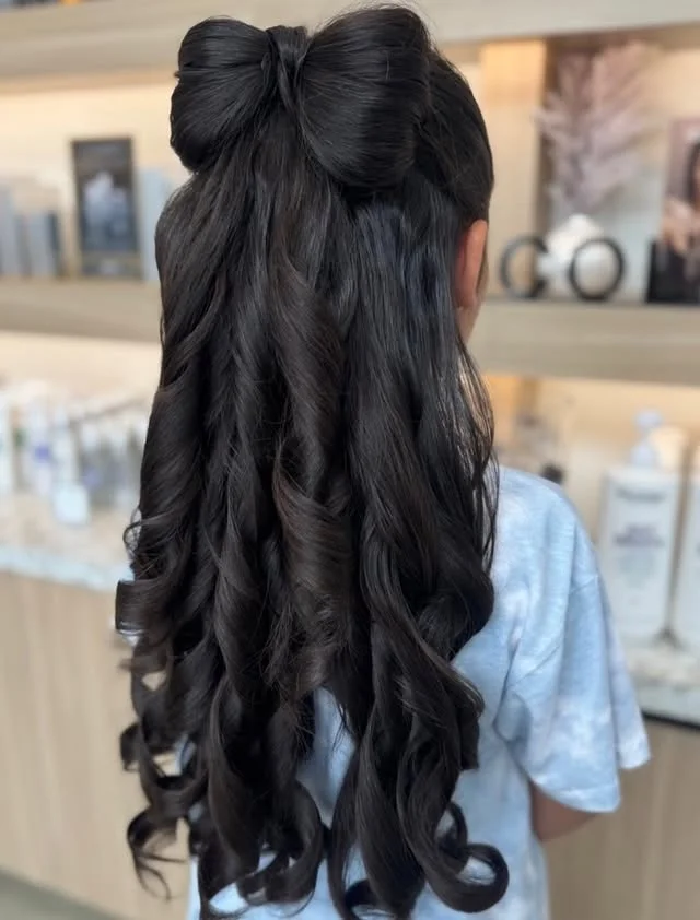 Top section of hair sculpted into a large bow at the crown with flowing curls