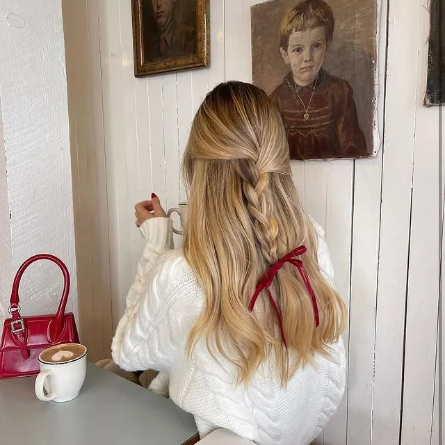 Half-up blonde braid finished with a small red velvet ribbon bow
