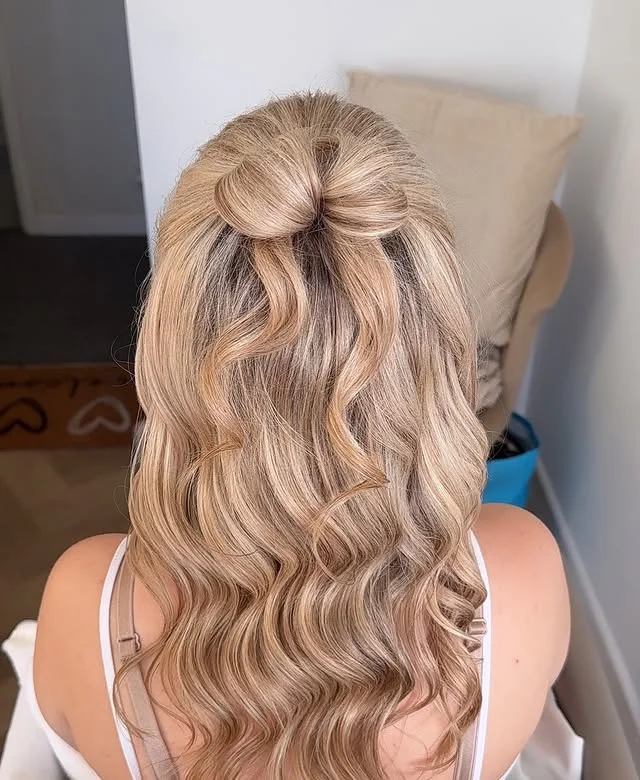 Blonde half-up half-down style with a small bow and soft waves