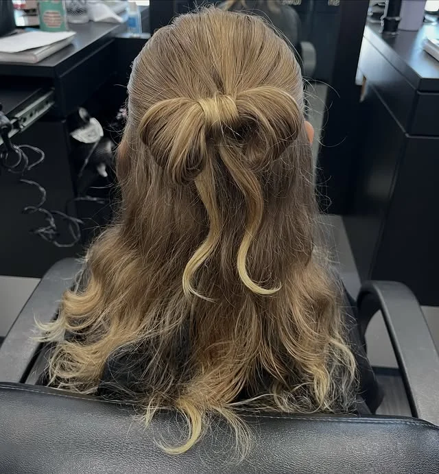 Small decorative bow made from woven hair at the crown of a half-up style