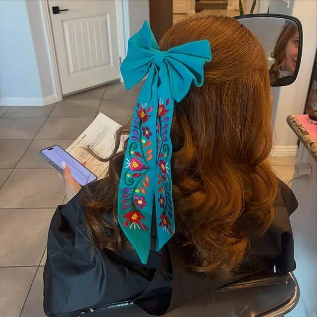 Half-up half-down wavy hair with a large embroidered fabric bow at the crown