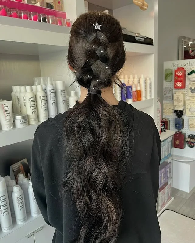 A woman with long dark voluminous hair in a low ponytail with a thick braided section at the crown adorned with rhinestones and a star clip.