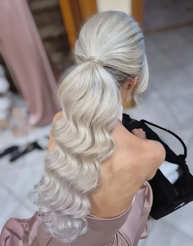 A woman with very long platinum blonde wavy hair in a high ponytail, photographed from behind.