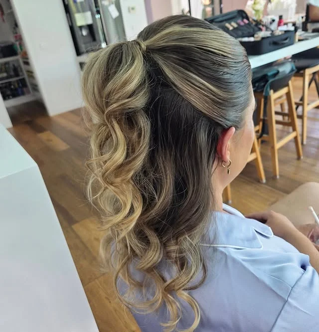 A woman with blonde curly hair pulled into a high ponytail, seen from behind.