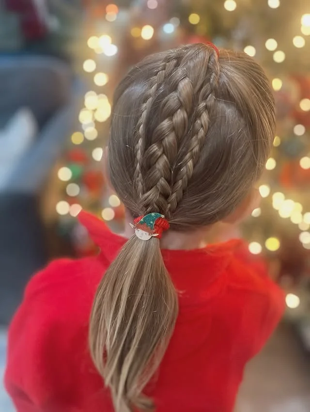 A young girl with three neat French braids converging into a low ponytail tied with a colorful band.