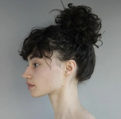 Woman with a messy curly topknot and fringe