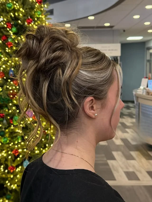 Voluminous textured high bun with loose face-framing strands, photographed near a Christmas tree.