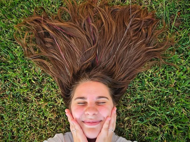 Overhead view of long brown hair spread on grass with pink and silver tinsel strands woven through.
