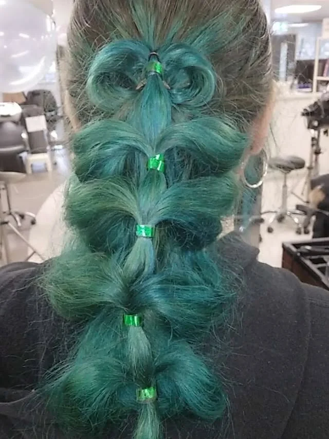 Teal-dyed hair styled into layered bubble sections resembling a Christmas tree with green bands.