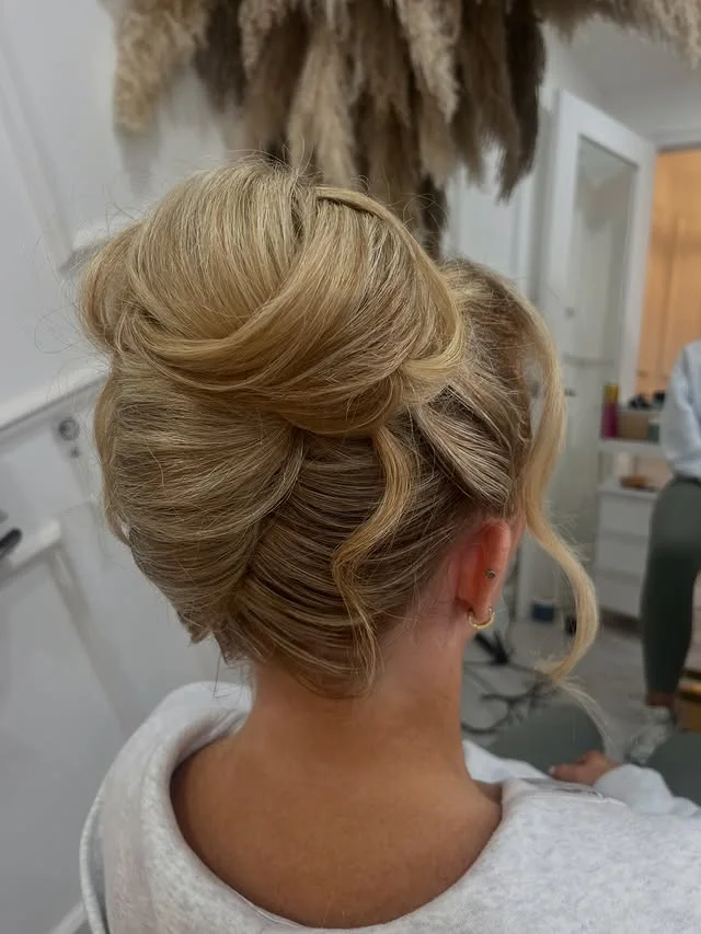 Smooth blonde wrapped bun photographed from the side in a salon setting.