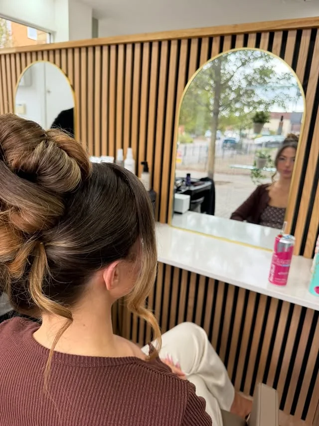 Dramatic twisted high bun on dark brown hair with face-framing pieces, in a salon.