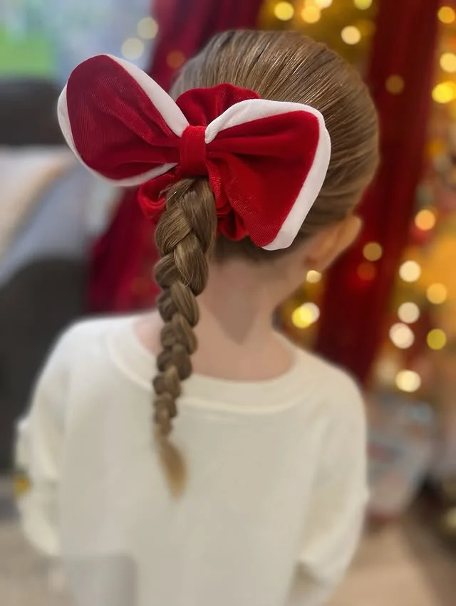 Child's neat low braid topped with a large red-and-white Santa-style bow.