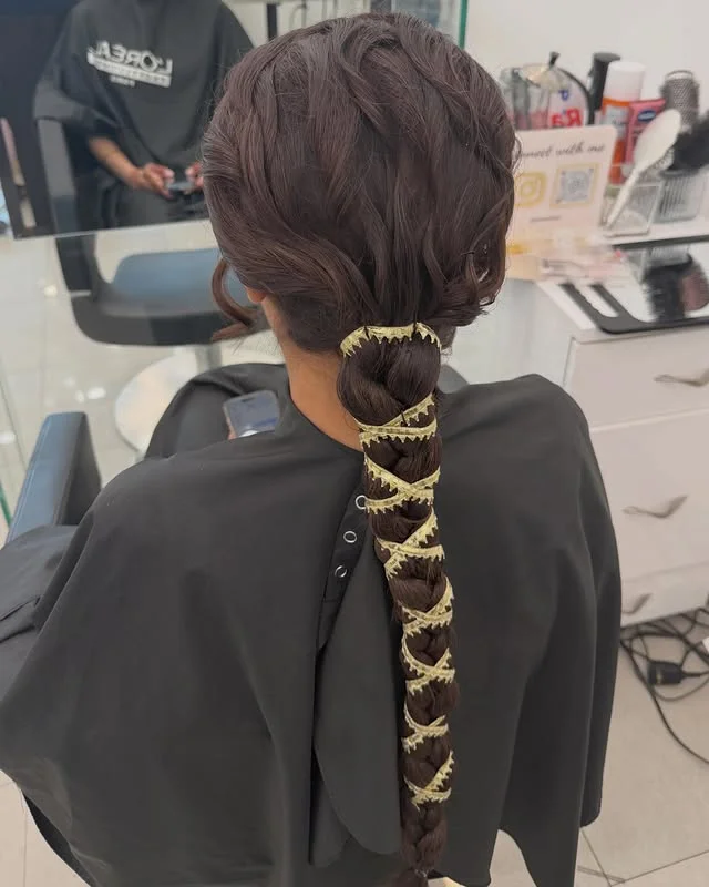 Braided ponytail with a gold ribbon woven down its length, viewed from behind.