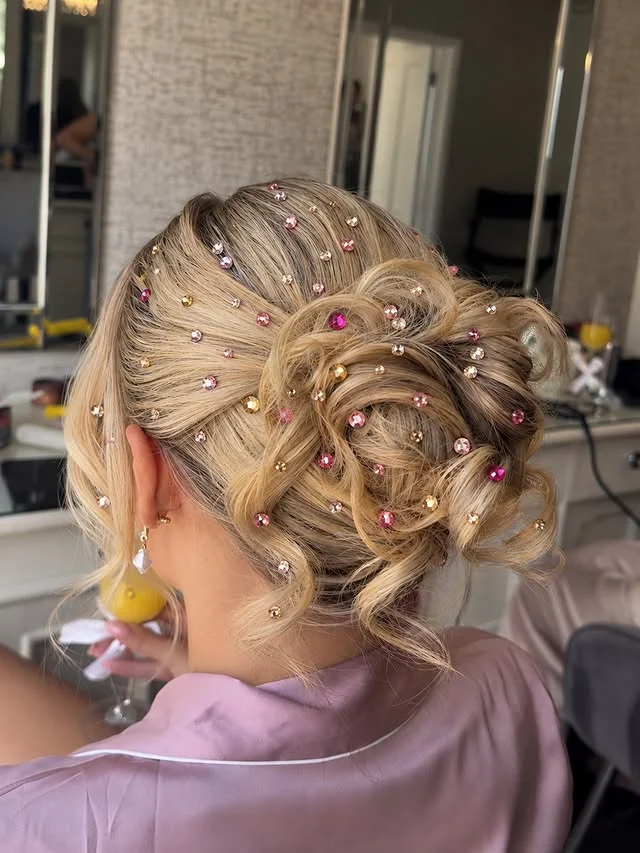 Rear view of a blonde curled updo scattered with pink and gold rhinestone hair gems.